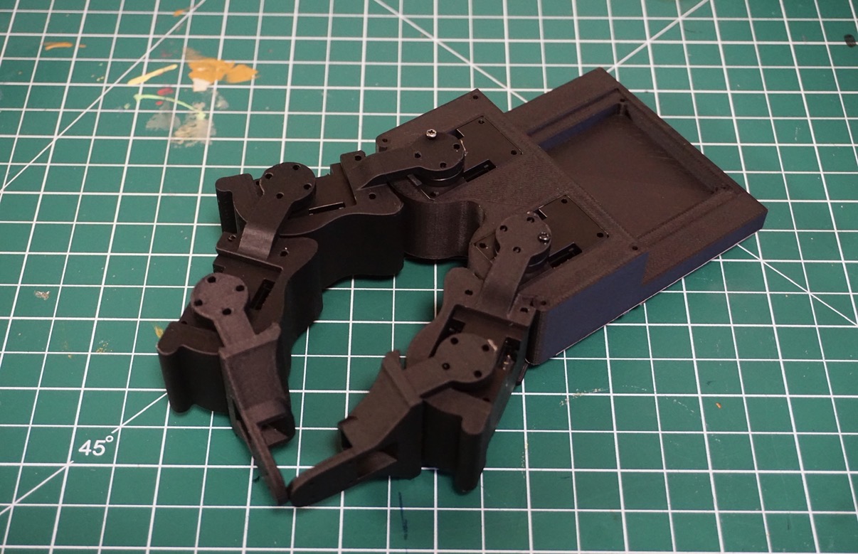 Black robotic hand mechanism prototype on a green cutting mat
