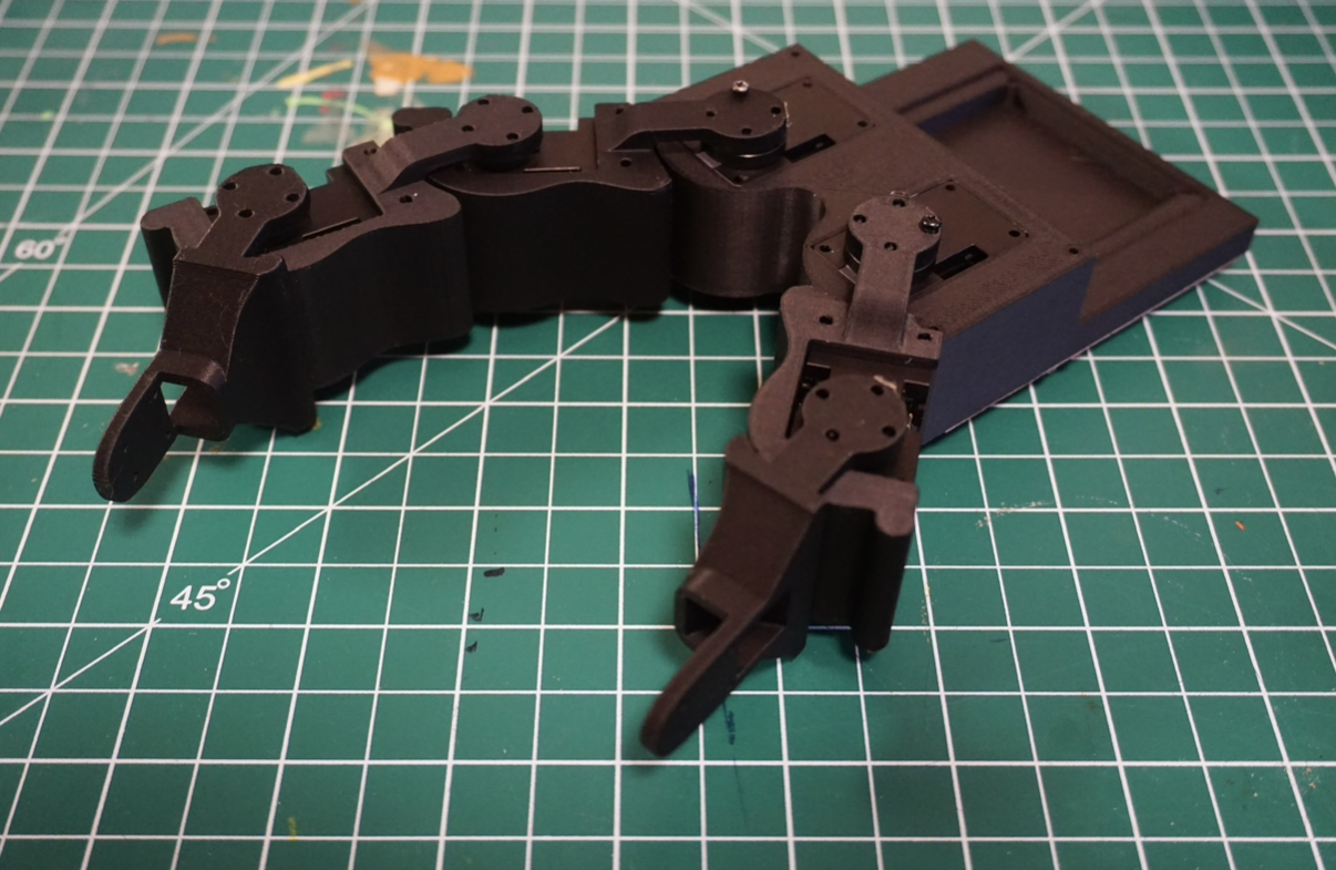 Black articulated gripper prototype on a green cutting mat